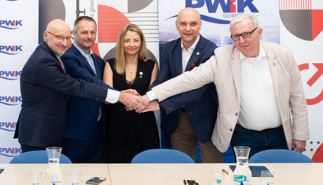 Technologia będzie działała w oparciu o odzysk ciepła ze ścieków oczyszczonych opuszczających Centralną Oczyszczalnię Ścieków. Ciepło zawarte w ściekach zostanie odebrane przez wymienniki ciepła, a następnie przekazane do wielkoskalowej pompy ciepła. Urządzenie podniesie temperaturę energii do parametrów wymaganych przez miejską sieć ciepłowniczą i przekaże ją do systemu PEC Gliwice. Kluczową rolą integratora będzie zapewnienie stabilnej współpracy pomiędzy infrastrukturą oczyszczalni, układem pomp ciepła oraz miejskim systemem ciepłowniczym. Obejmuje to także przygotowanie zaawansowanego systemu automatyki odpowiedzialnego za optymalizację pracy instalacji w zależności od temperatur zewnętrznych, zapotrzebowania sieci oraz parametrów ścieków. – Konsekwentnie rozwijamy działania związane z dywersyfikacją źródeł ciepła i zwiększaniem niezależności energetycznej miasta. Poszukujemy lokalnych potencjałów energetycznych, które pozwolą nam produkować ciepło w sposób bardziej efektywny, stabilny i przyjazny środowisku. Wykorzystanie ciepła zawartego w ściekach to przykład nowoczesnego podejścia do ciepłownictwa, które jednocześnie zwiększa bezpieczeństwo dostaw dla mieszkańców i ogranicza konieczność korzystania z paliw kopalnych oraz surowców dostarczanych z zewnątrz – tłumaczy Krzysztof Szaliński, prezes PEC Gliwice. Projekt ma charakter strategiczny dla transformacji energetycznej Gliwic. Dzięki wykorzystaniu ciepła odpadowego miasto zwiększy udział odnawialnych i niskoemisyjnych źródeł energii w ciepłownictwie systemowym, jednocześnie poprawiając bezpieczeństwo energetyczne oraz efektywność produkcji ciepła. Inwestycja wpisuje się również w europejskie kierunki dekarbonizacji sektora ciepłowniczego i rozwoju gospodarki obiegu zamkniętego. Szacowana wartość całego przedsięwzięcia wynosi około 100–120 mln zł. Projekt jest współfinansowany przez Narodowy Fundusz Ochrony Środowiska i Gospodarki Wodnej. Inwestycja ma być gotowa z końcem 2027 roku. UWAGA! NA ZDJĘCIU UCZESTNICZY UROCZYSTOŚCI PODPISANIA UMÓW. OD LEWEJ: Paweł Bachorz (wiceprezes Grupy KDM), Jakub Kowalczyk (wiceprezes Grupy KDM), Patrycja Jurkiewicz-Cygan (wiceprezes PEC-Gliwice ds. finansowych), Krzysztof Szaliński (prezes PEC-Gliwice), Tomasz Brągiel (prezes PWiK Gliwice – spółki na terenie, której inwestycja powstanie).